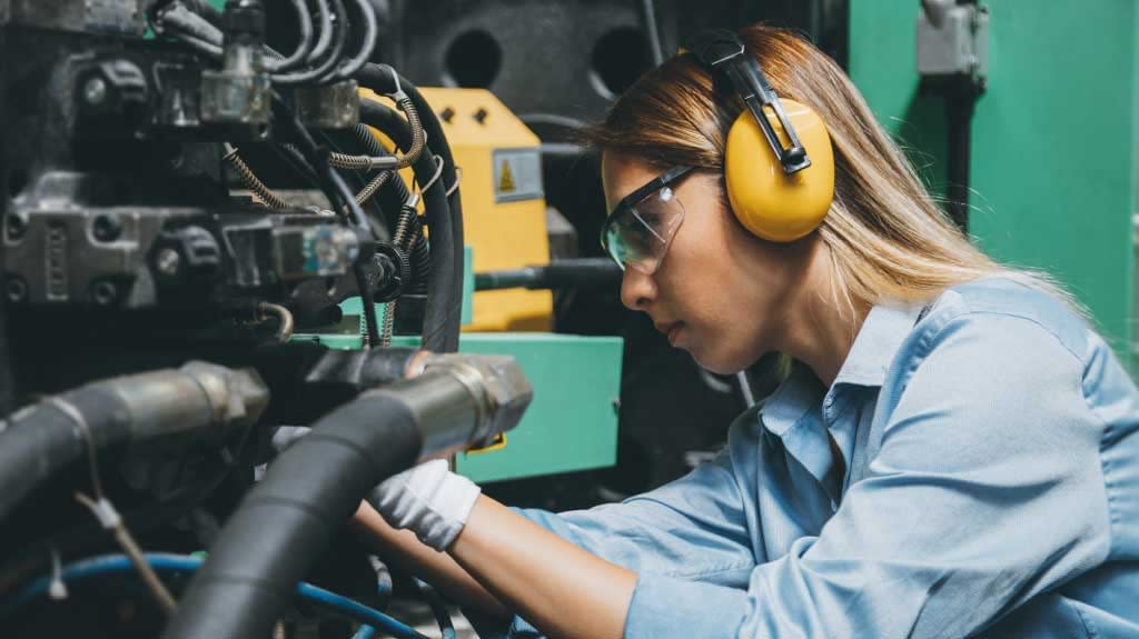 Close up side view portrait of young female technical repair engineer employee operating a production line industrial CNC machine and testing, installing, analyzing and fixing bolts it with hand tools for work at a modern factory plant building.