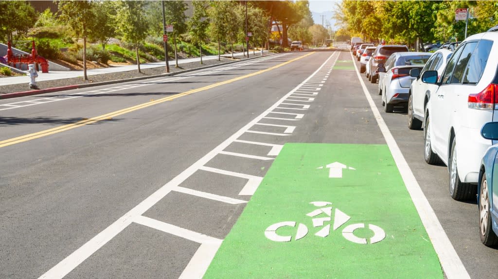 Bicycle lane along a road in a business park. Cars are parked along the lane