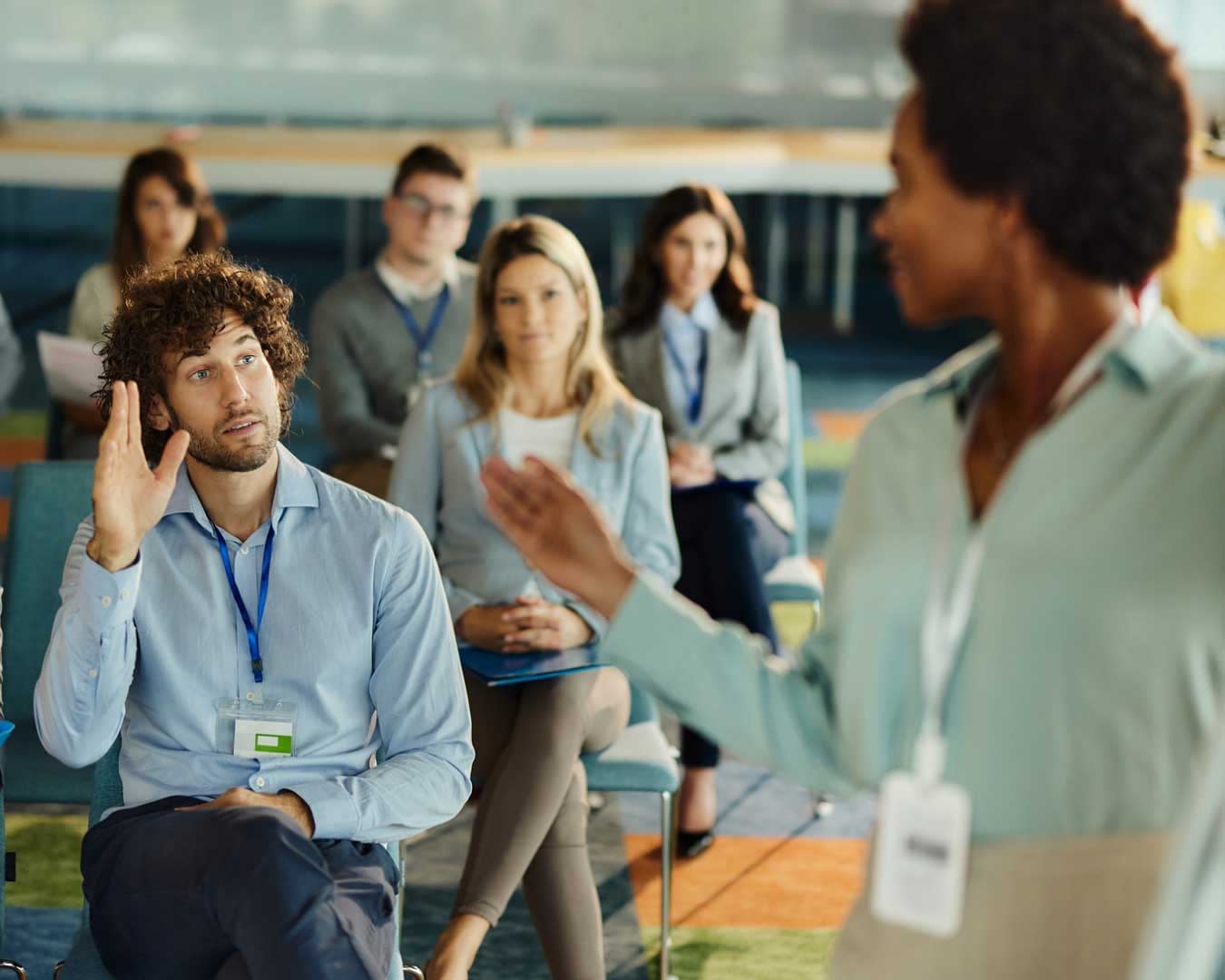 African woman leading training session. Young businessman is raising his hand to ask a question on education event with his colleagues in board room.