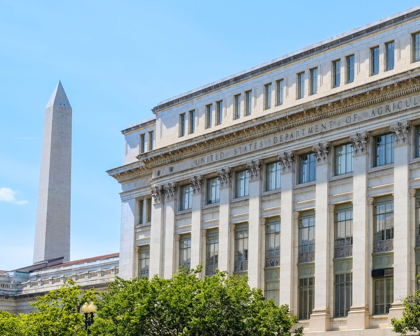 The Federal Department of Agriculture building in Washington DC on a clear blue sky day with Washington Monument in the background.