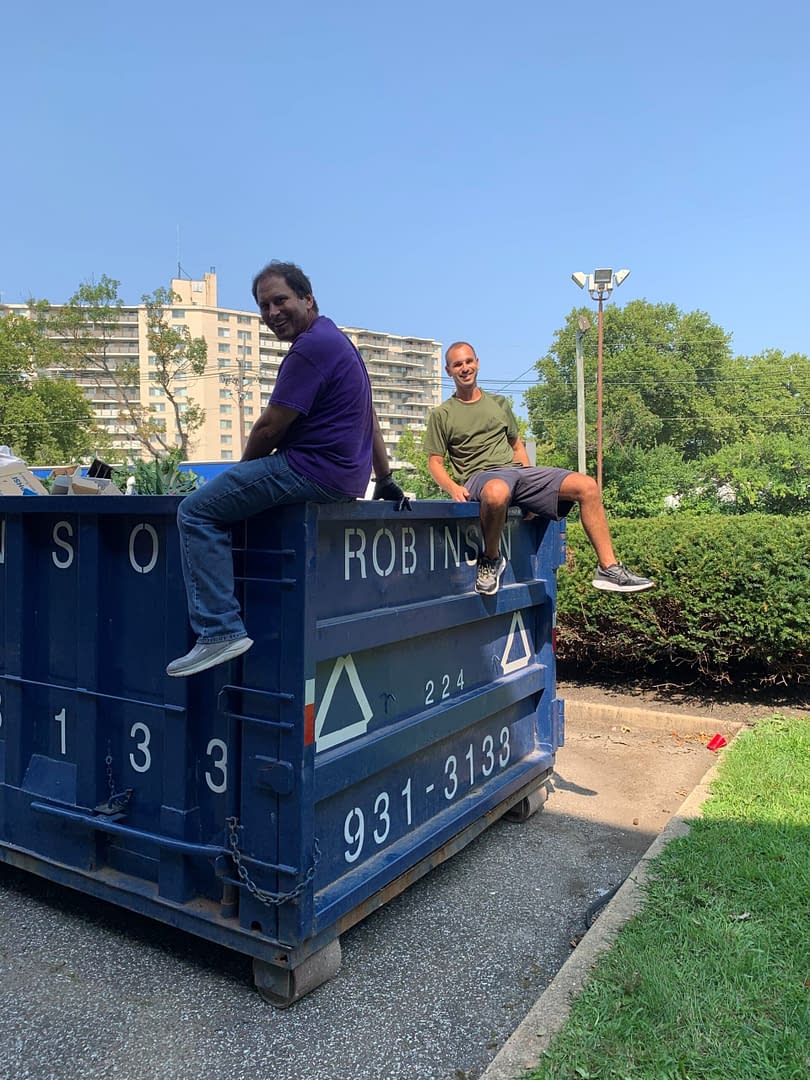 Two UTRS employees sitting on dumpster while helping clear out old headquarter building.